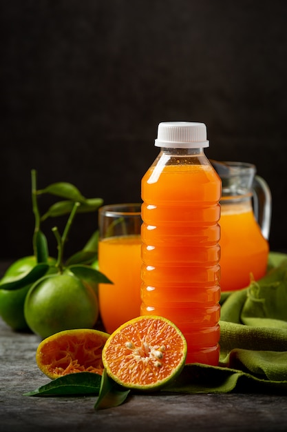 Un vaso de jugo de naranja y fruta fresca en el piso con cubitos de hielo.