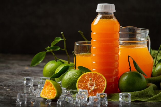 Un vaso de jugo de naranja y fruta fresca en el piso con cubitos de hielo.