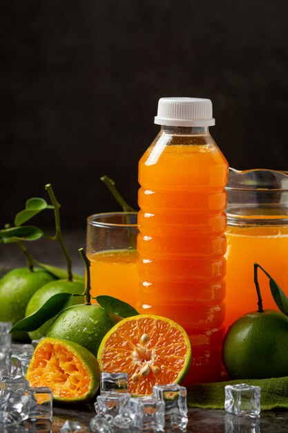 Un vaso de jugo de naranja y fruta fresca en el piso con cubitos de hielo.