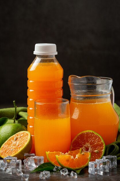 Un vaso de jugo de naranja y fruta fresca en el piso con cubitos de hielo.