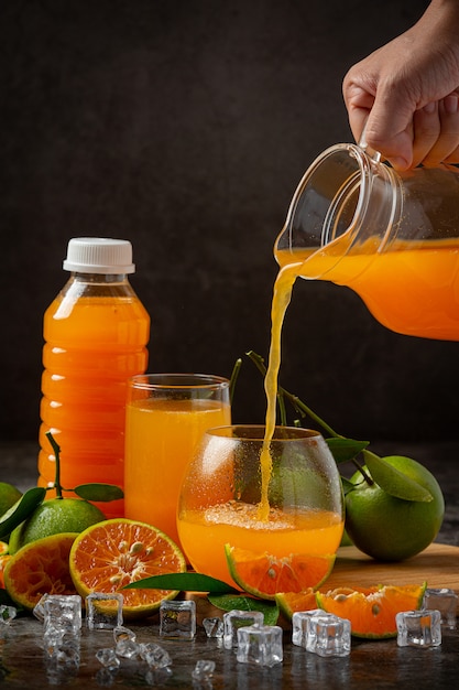 Un vaso de jugo de naranja y fruta fresca en el piso con cubitos de hielo.