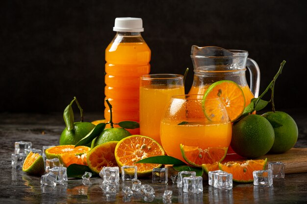 Un vaso de jugo de naranja y fruta fresca en el piso con cubitos de hielo.