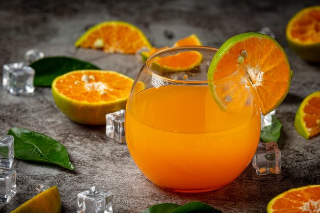 Un vaso de jugo de naranja y fruta fresca en el piso con cubitos de hielo.