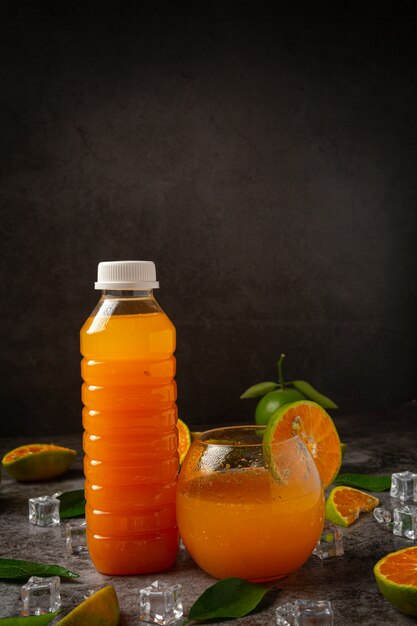 Un vaso de jugo de naranja y fruta fresca en el piso con cubitos de hielo.