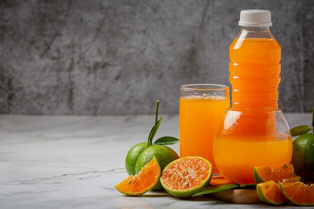 Un vaso de jugo de naranja y fruta fresca en el piso con cubitos de hielo.