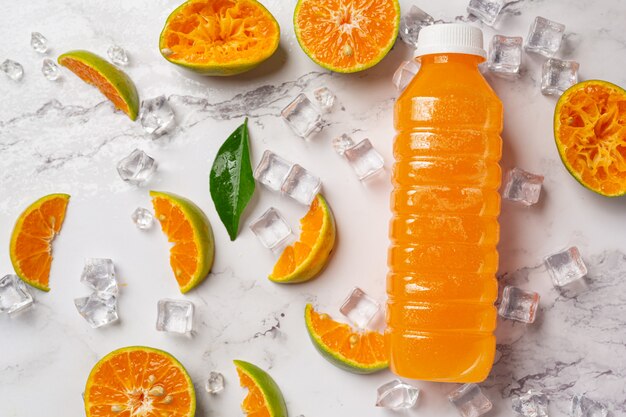 Un vaso de jugo de naranja y fruta fresca en el piso con cubitos de hielo.