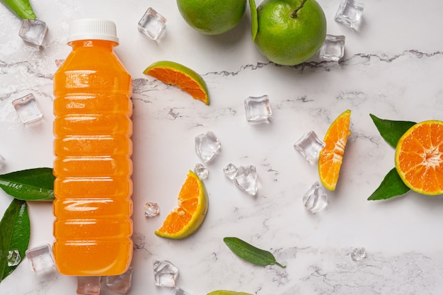 Un vaso de jugo de naranja y fruta fresca en el piso con cubitos de hielo.