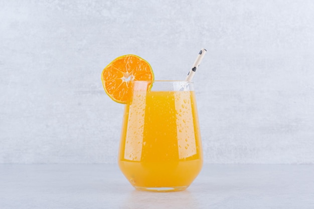 Un vaso de jugo de naranja con paja sobre piedra