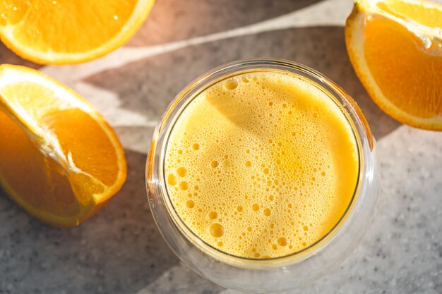 Un vaso de jugo de naranja recién exprimido y naranjas en la mesa de la cocina