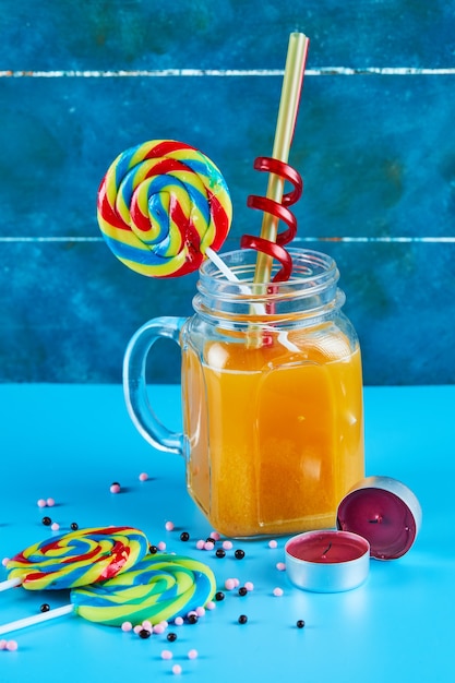 Foto gratuita un vaso de jugo con paletas de colores sobre superficie azul.