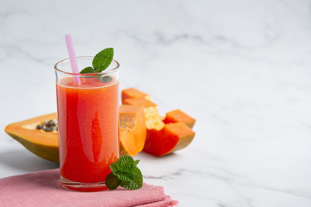 Vaso de jugo de papaya puesto sobre piso de mármol blanco