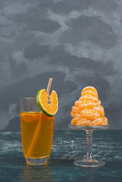 Vaso de jugo y rodajas de mandarina en la pared de mármol.
