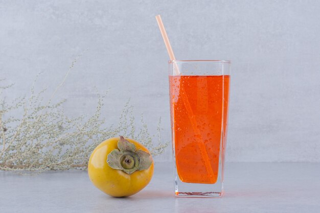 Un vaso de jugo rojo con caqui sobre fondo de piedra. Foto de alta calidad