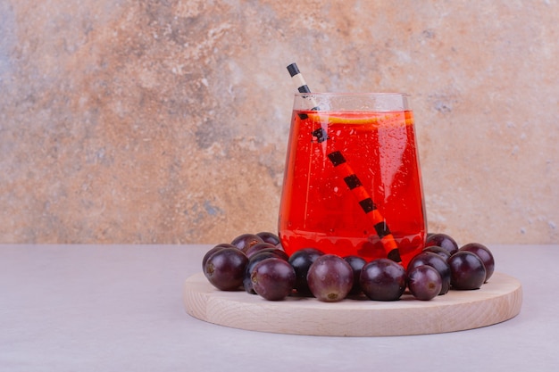 Un vaso de jugo rojo con cerezas en una tabla de madera