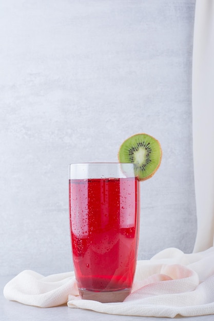 Un vaso de jugo rojo sobre un mantel con una rodaja de kiwi. Foto de alta calidad