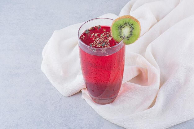 Un vaso de jugo rojo sobre un mantel con una rodaja de kiwi. Foto de alta calidad