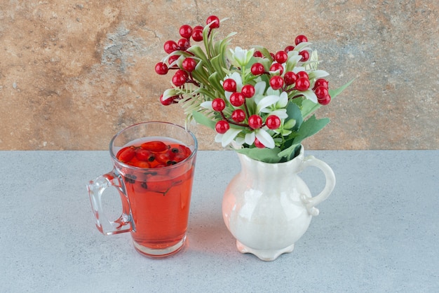 Vaso de jugo con rosa mosqueta y flores artificiales en el cuadro azul. Foto de alta calidad