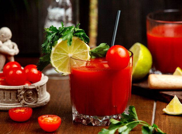 Un vaso de jugo de tomate adornado con tomate cherry, limón y perejil.