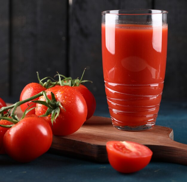 Un vaso de jugo de tomate, tomates enteros y cortados.