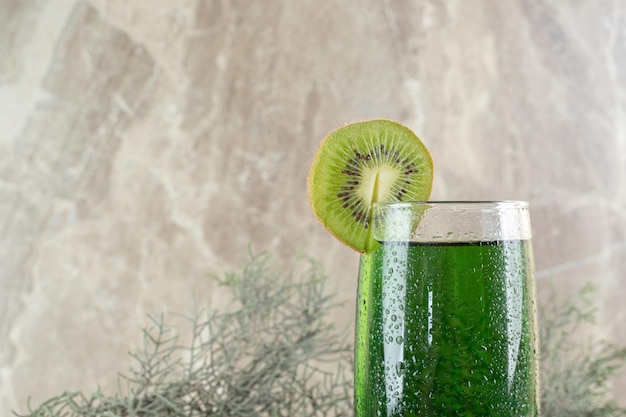 Vaso de jugo verde con rodajas de kiwi y rama de pino