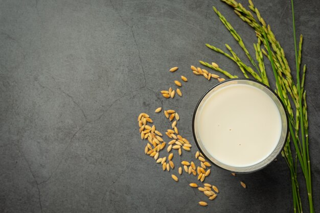 Vaso de leche de arroz con planta de arroz y semillas de arroz en piso oscuro