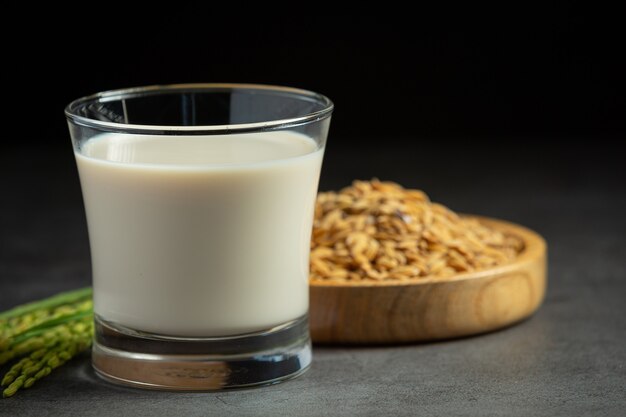 Vaso de leche de arroz con planta de arroz y semillas de arroz en piso oscuro