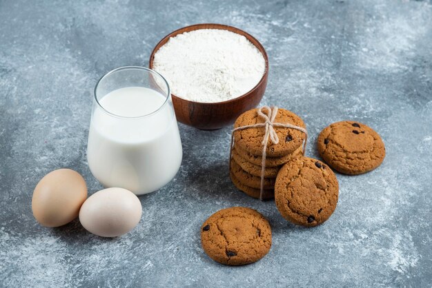 Un vaso de leche caliente con deliciosas galletas sobre una mesa gris.