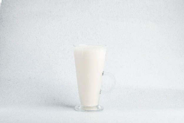Un vaso de leche en un fondo blanco con poca sombra.