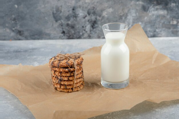 Vaso de leche fresca y pila de deliciosas galletas en hoja de papel.