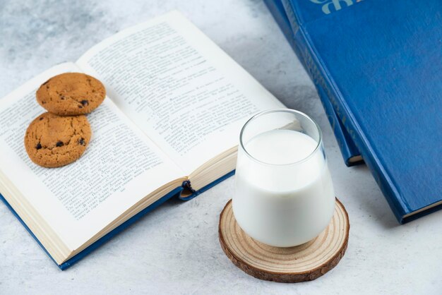 Un vaso de leche fría con galletas de chocolate y libros.