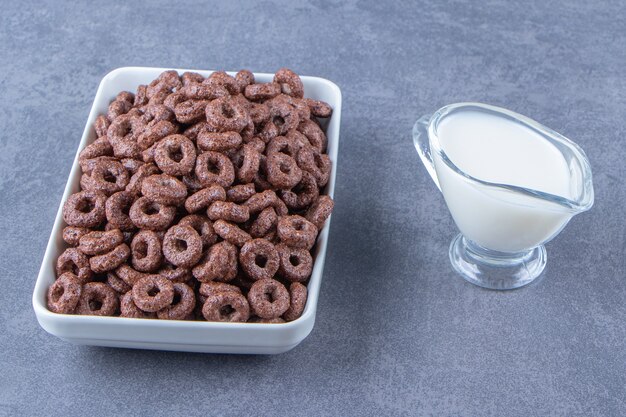 Un vaso de leche junto a los anillos de maíz en un recipiente de vidrio, sobre el fondo de mármol. Foto de alta calidad