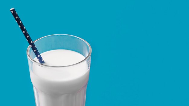 Vaso de leche con pajita sobre fondo azul