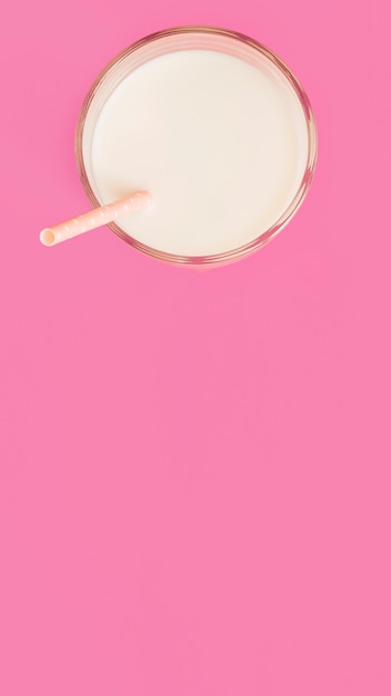 Vaso de leche saludable con pajita sobre el fondo rosa