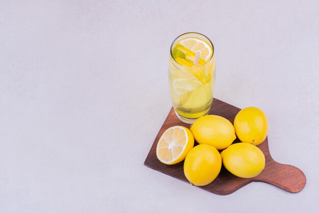 Un vaso de limonada con limones en una bandeja de madera