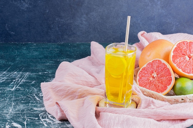 Un vaso de limonada con rodajas de limón y pomelos en la superficie de mármol.