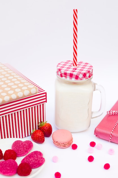 Vaso con líquido y tubo cerca de galletas, dulces, moras y regalos.