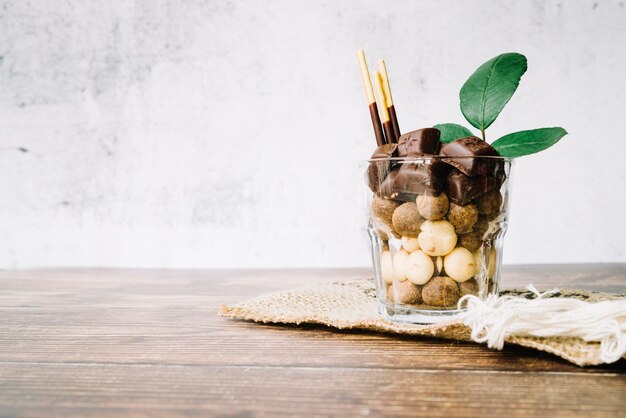 Vaso lleno de dulces chocolates y palo en la mesa de madera