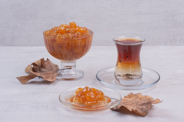 Vaso de mermelada de té y bayas en blanco con hojas.