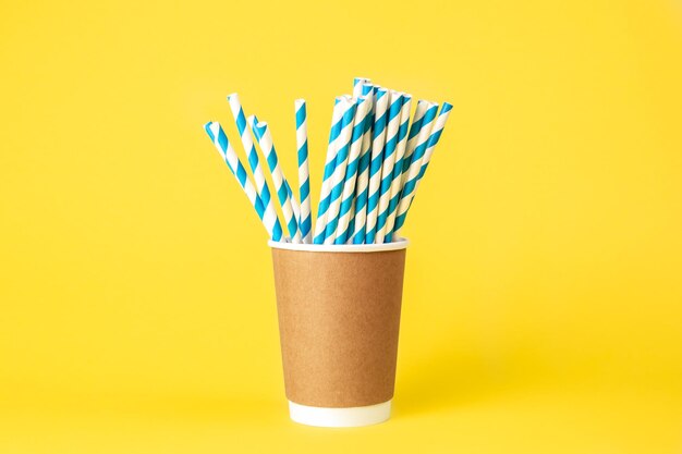 Vaso de papel desechable con pajitas de papel a rayas sobre un fondo amarillo