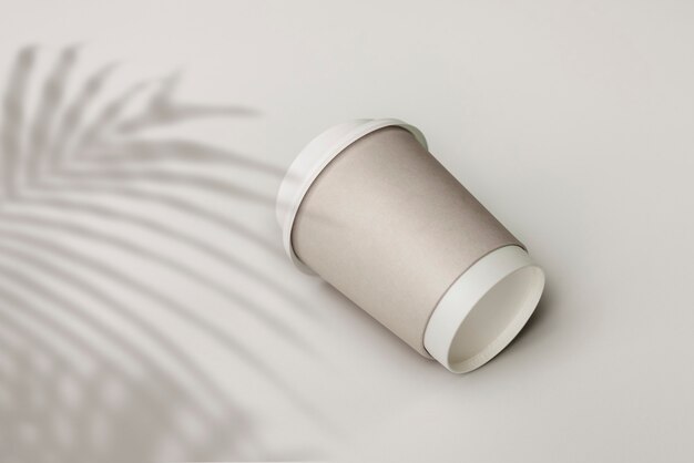 Vaso de papel gris con sombra de hoja de palma