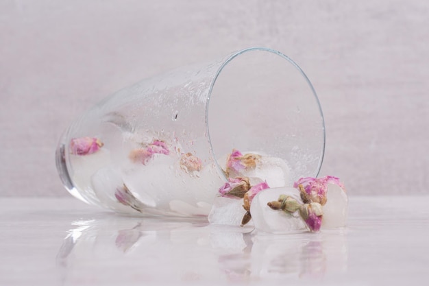 Un vaso con pequeñas rosas en hielo sobre mesa blanca.