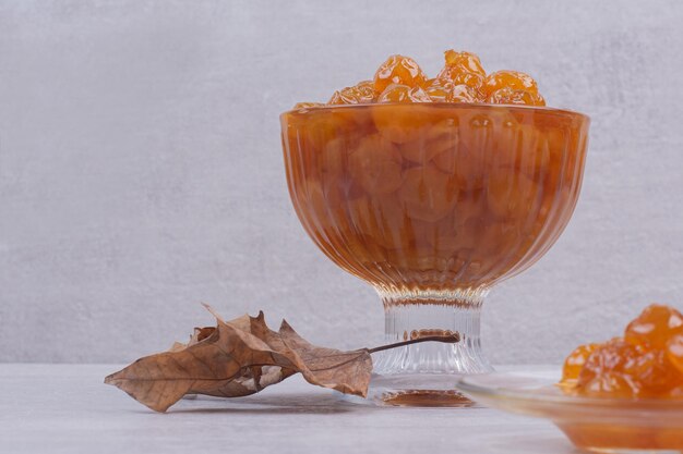 Un vaso de plato con mermelada y hojas sobre mesa blanca.