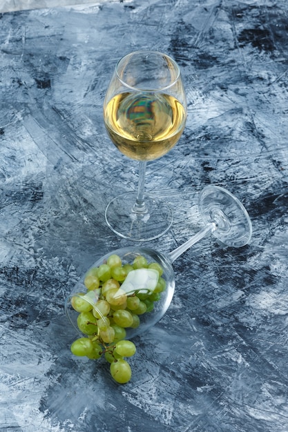 Vaso de primer plano de uvas blancas con vaso de whisky sobre fondo de mármol azul oscuro. vertical