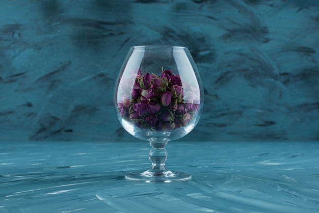 Foto gratuita vaso de rosas púrpuras secas colocadas sobre una superficie azul.