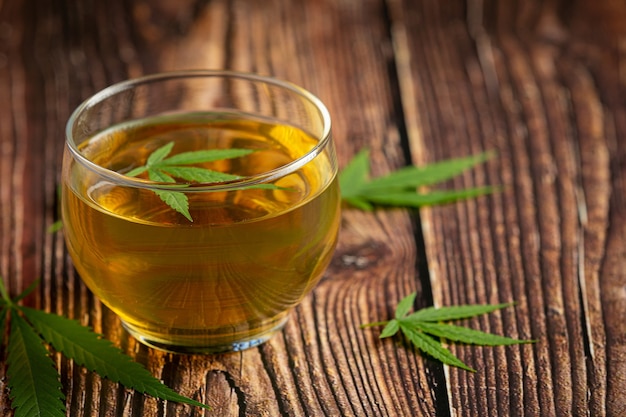 Vaso de té de cáñamo con hojas de cáñamo puesto sobre un piso de madera
