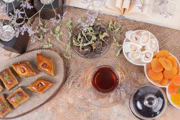 Vaso de té, dulces y baklavas tradicionales en mesa de mármol.