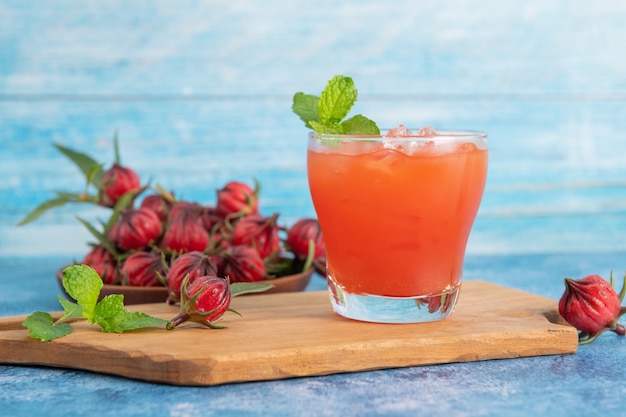 Vaso de té helado de roselle con fruta fresca de roselle en la mesa de madera para un concepto saludable de bebida a base de hierbas. té orgánico de hierbas para una buena salud.