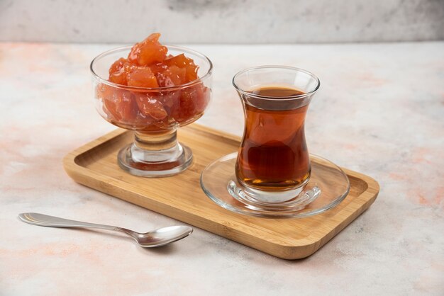 Vaso de té negro y mermelada de membrillo en placa de madera.