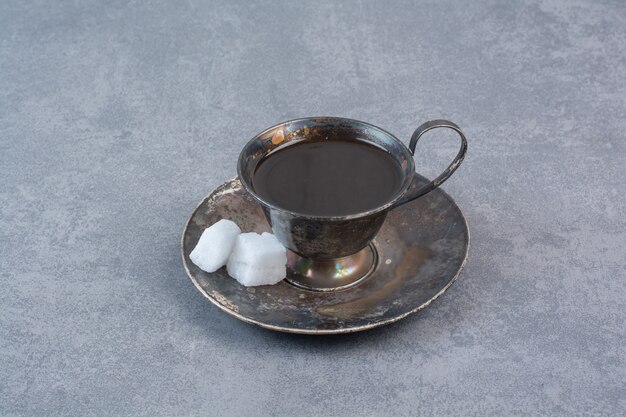 Un vaso de té oscuro de aroma en mesa gris.
