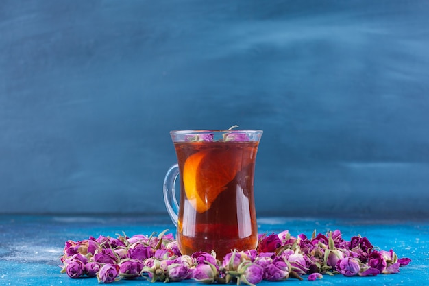 Vaso de té con rosas en ciernes colocadas sobre la mesa azul.